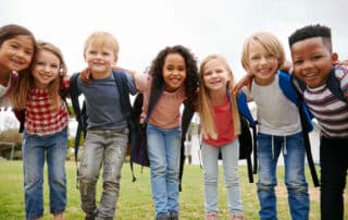 Excited elementary school children carrying backpacks smiling on first day of school.