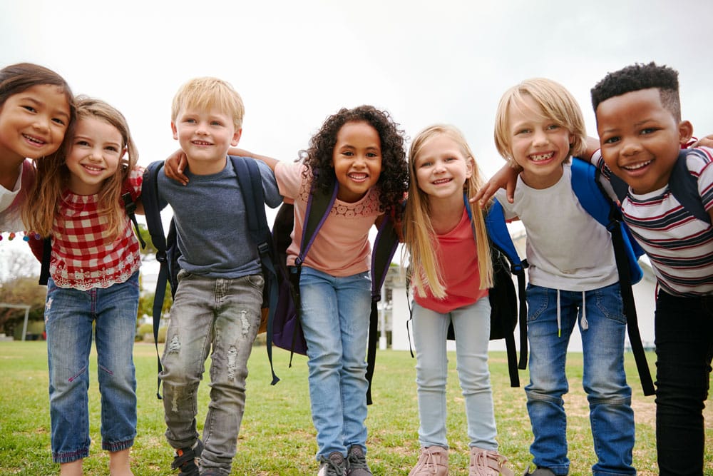 Excited elementary school children carrying backpacks smiling on first day of school.